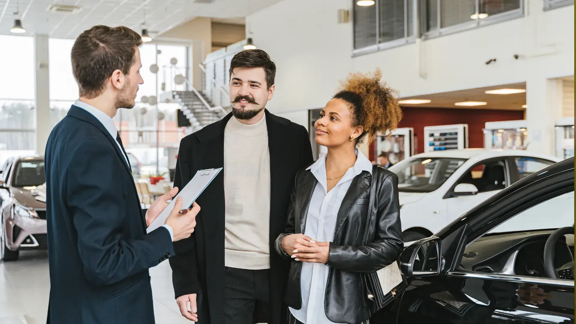 A man is talking to a woman and a man in a car showroom.