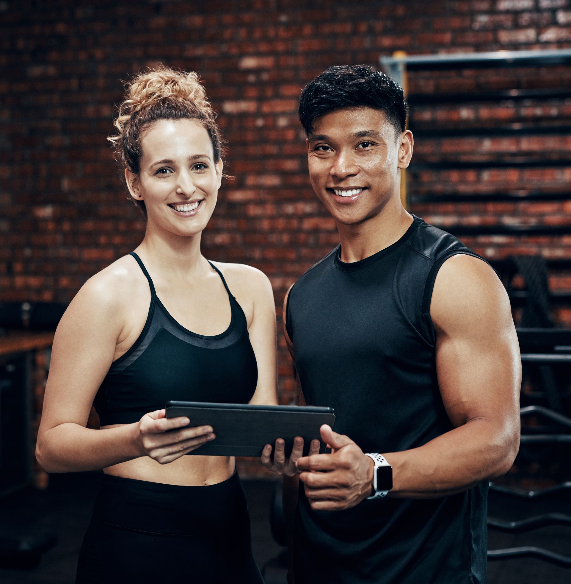 A man and a woman are standing next to each other in a gym holding a tablet.
