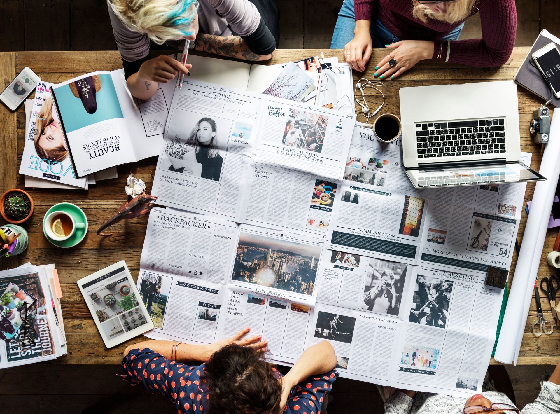 A group of people are sitting around a table looking at newspapers.