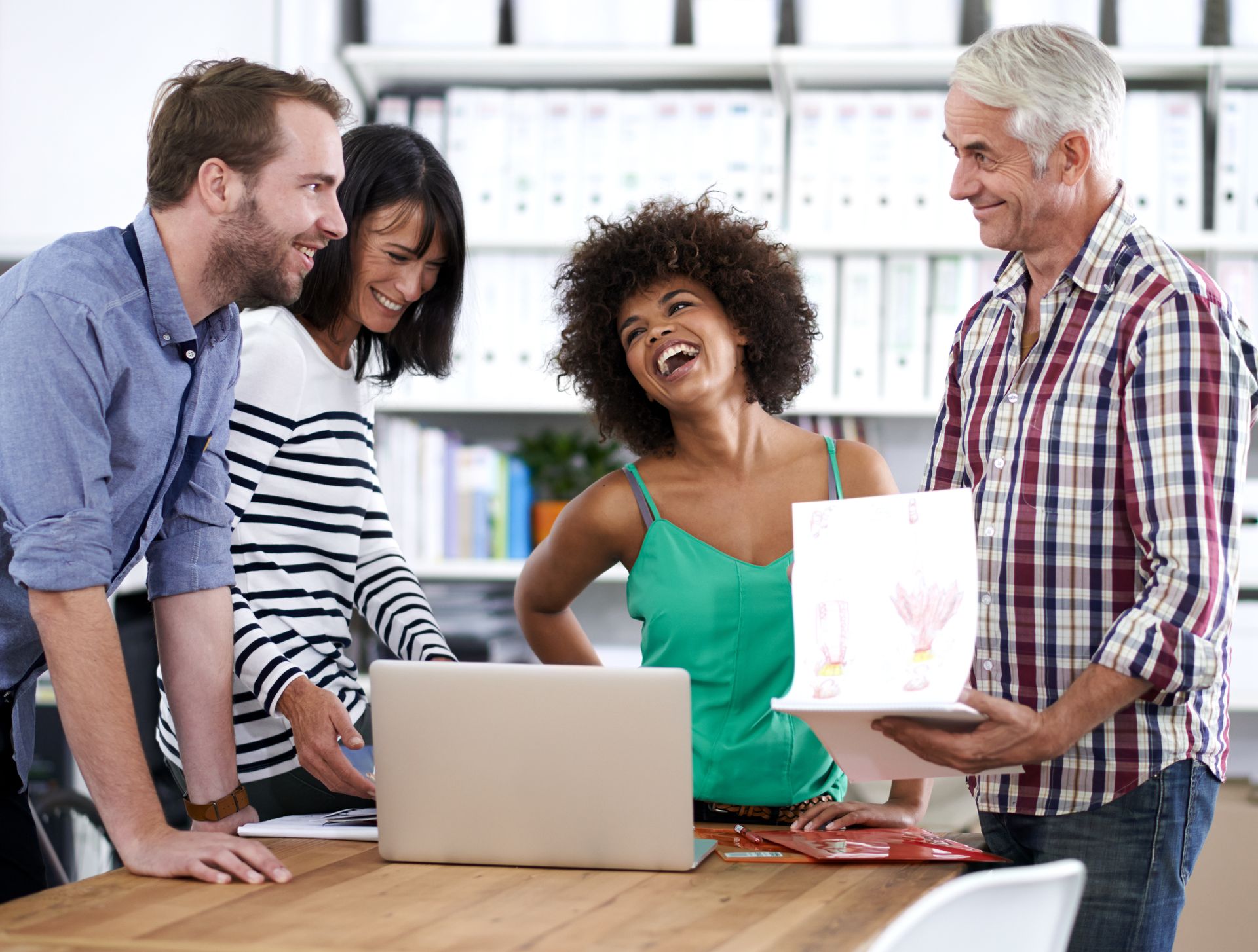 A group of people are standing around a table looking at a laptop.