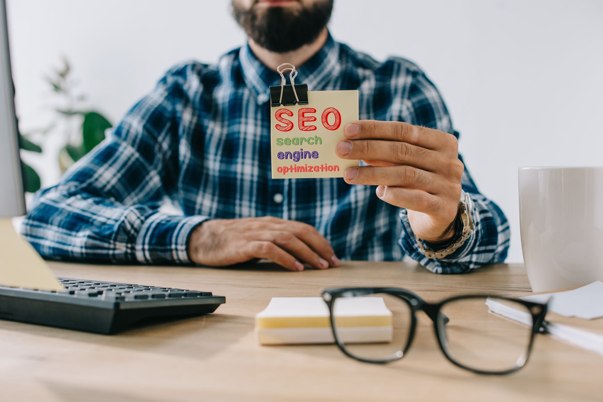 A man is sitting at a desk holding a piece of paper with the word seo written on it.