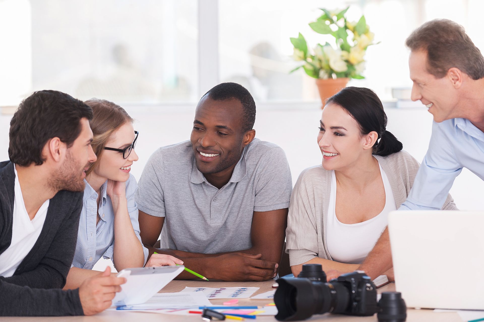 A group of people are sitting around a table looking at a laptop.
