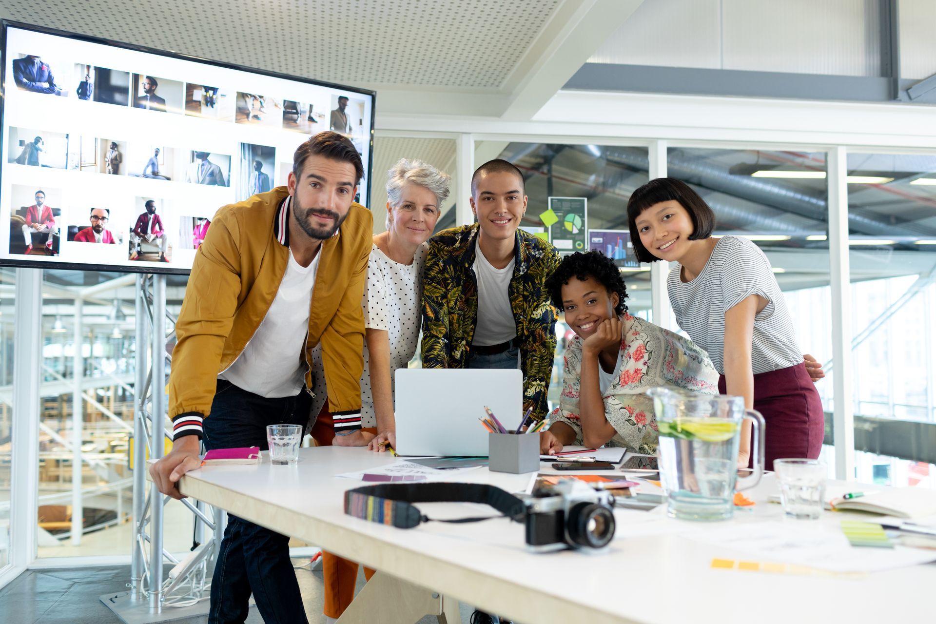 A group of people are standing around a table with a laptop and a camera.
