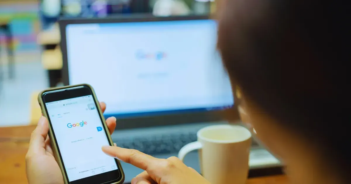 A person is holding a cell phone in front of a laptop computer.