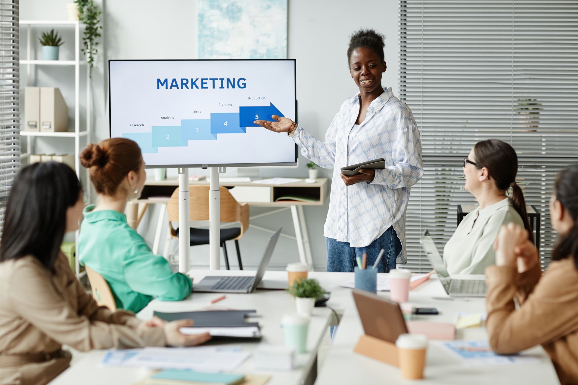 A woman is giving a presentation to a group of people sitting around a table.