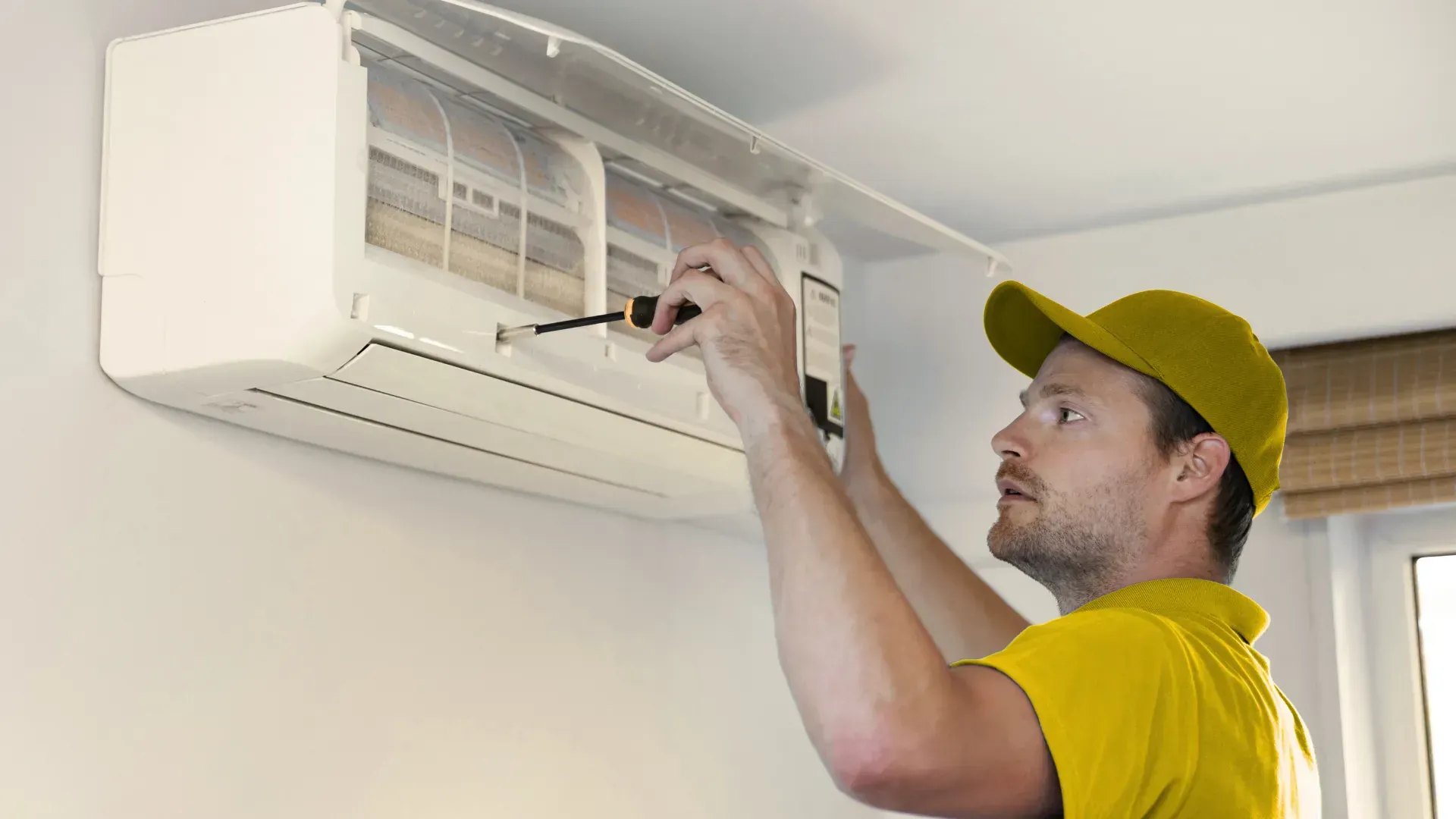 A man is fixing an air conditioner with a screwdriver.