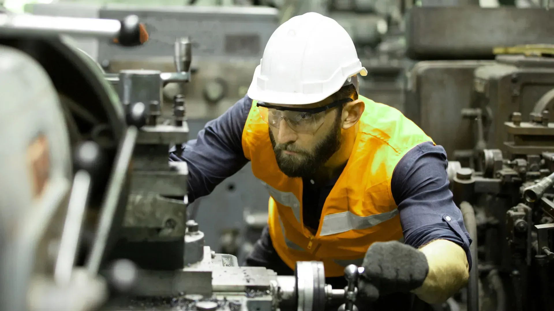 A man wearing a hard hat and safety vest is working on a machine in a factory.