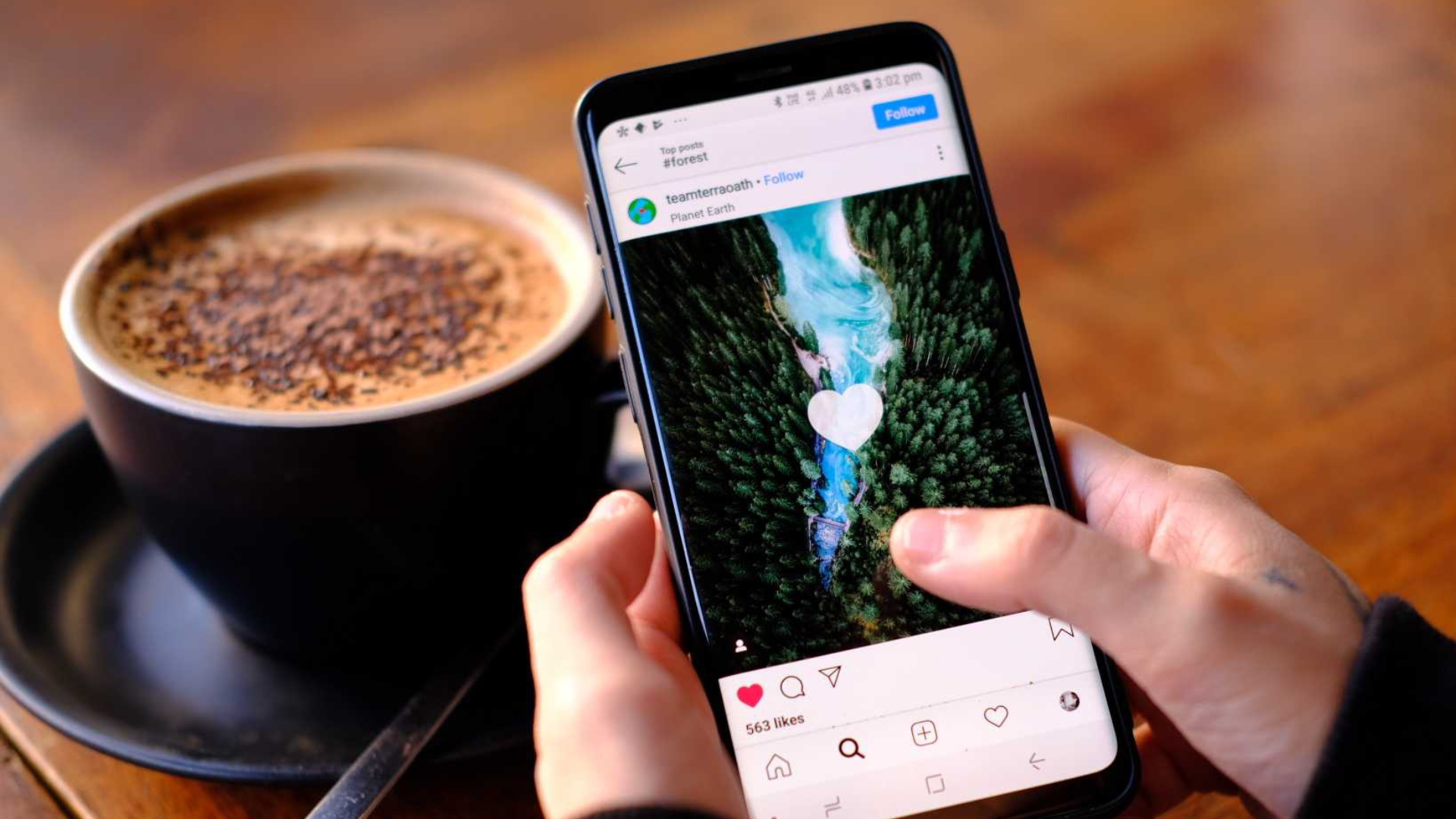 A person is holding a cell phone in front of a cup of coffee.