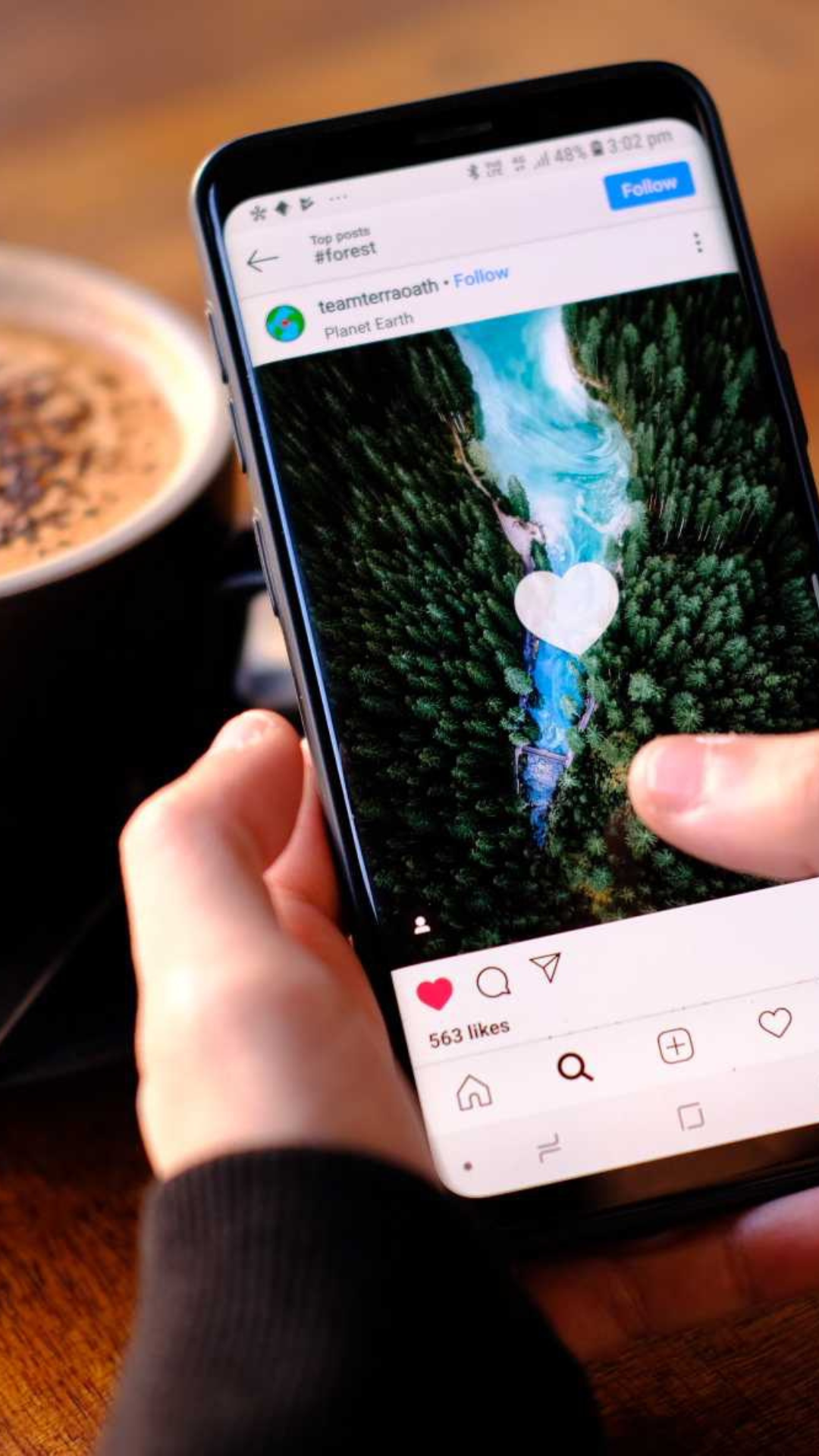 A person is holding a cell phone in front of a cup of coffee.