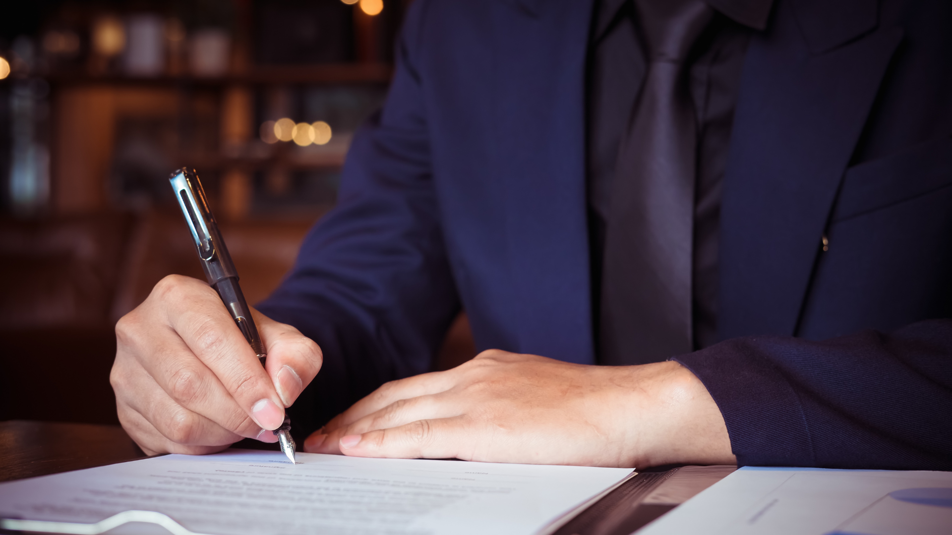 A man in a suit and tie is signing a document with a pen.