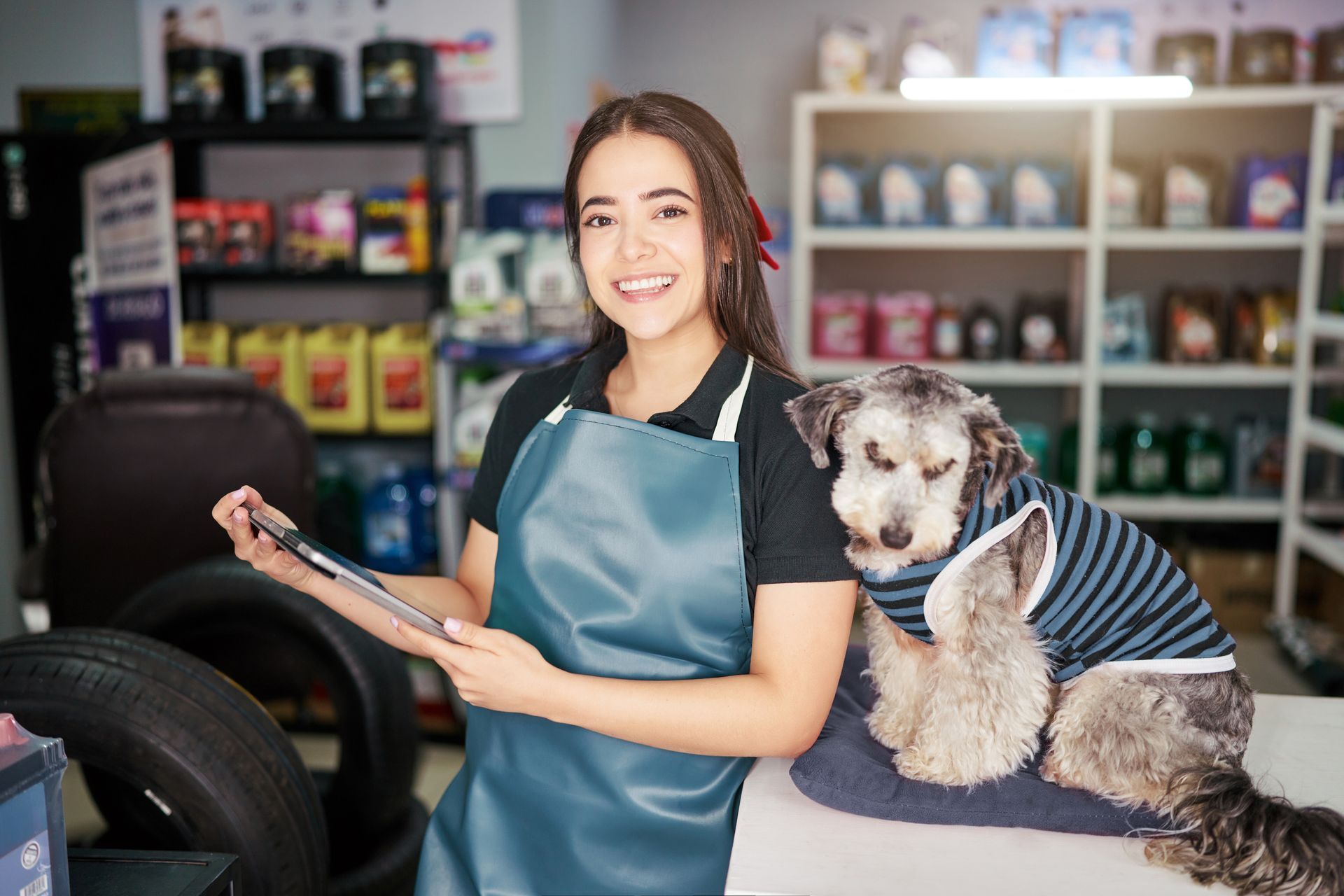 A woman is holding a tablet next to a small dog in a garage.
