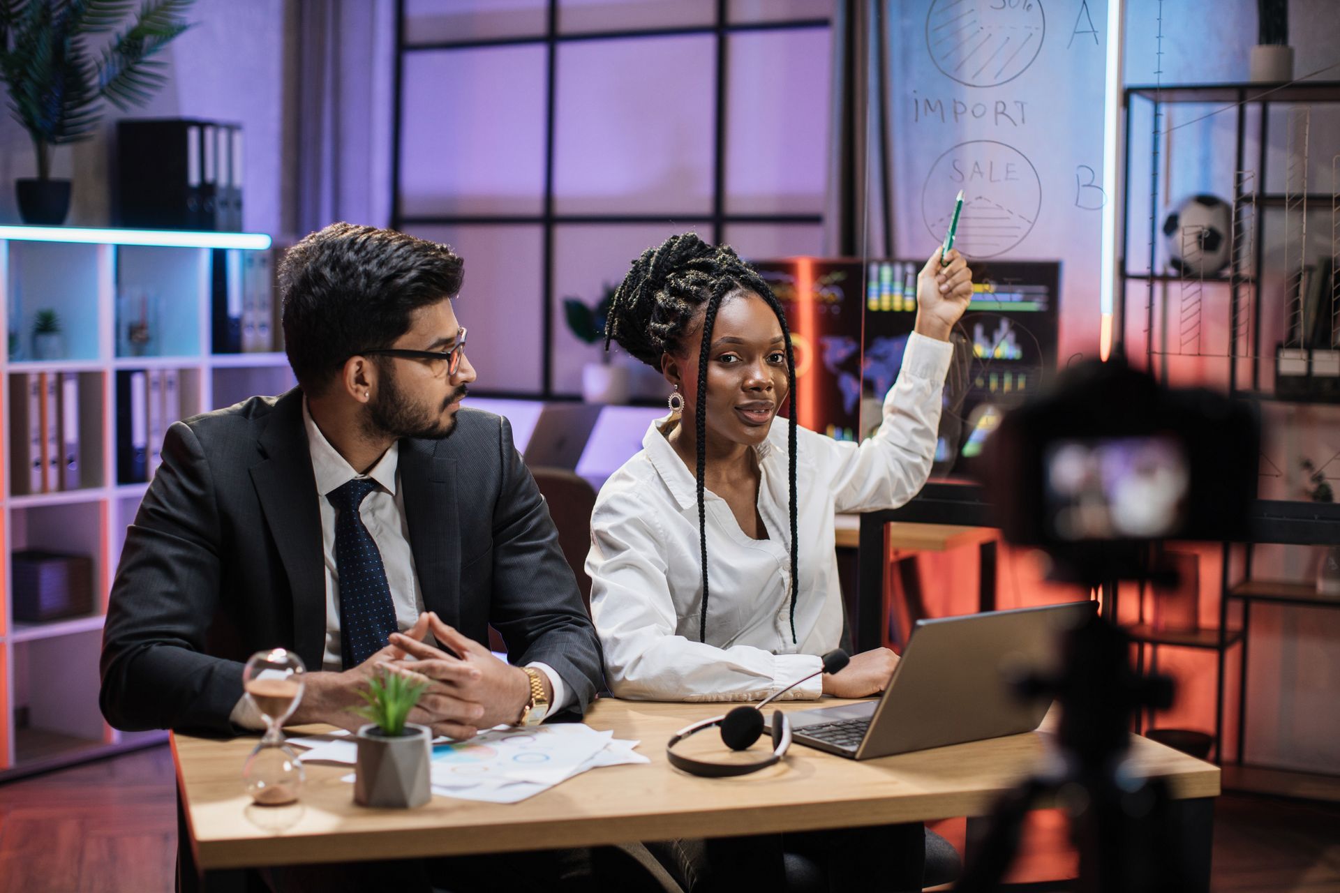 A man and a woman are sitting at a table in front of a camera.