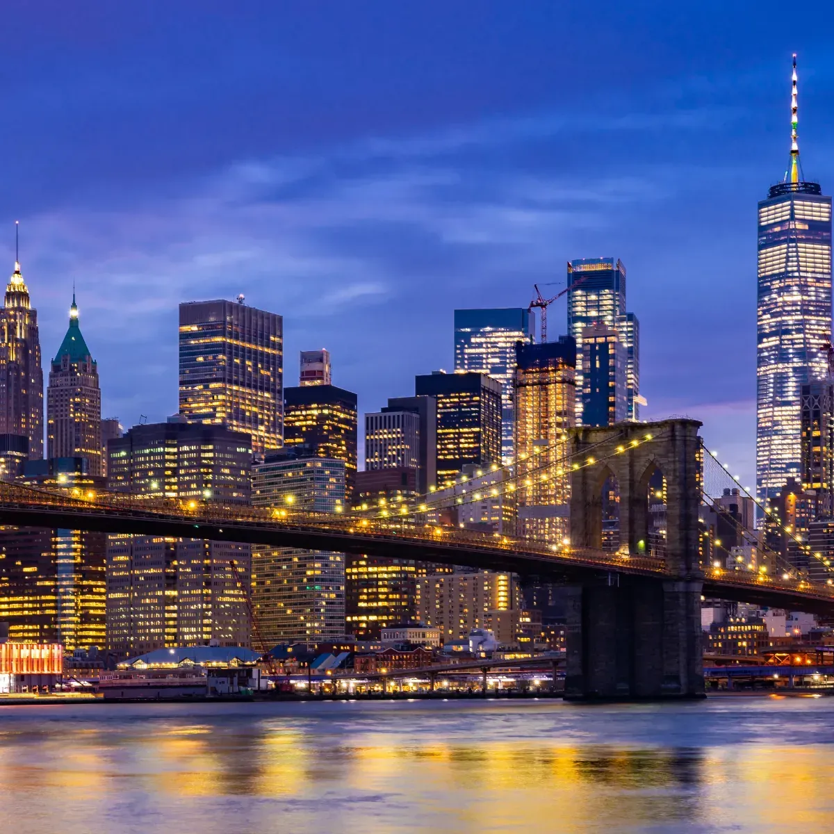 A bridge over a body of water in front of a city skyline at night.