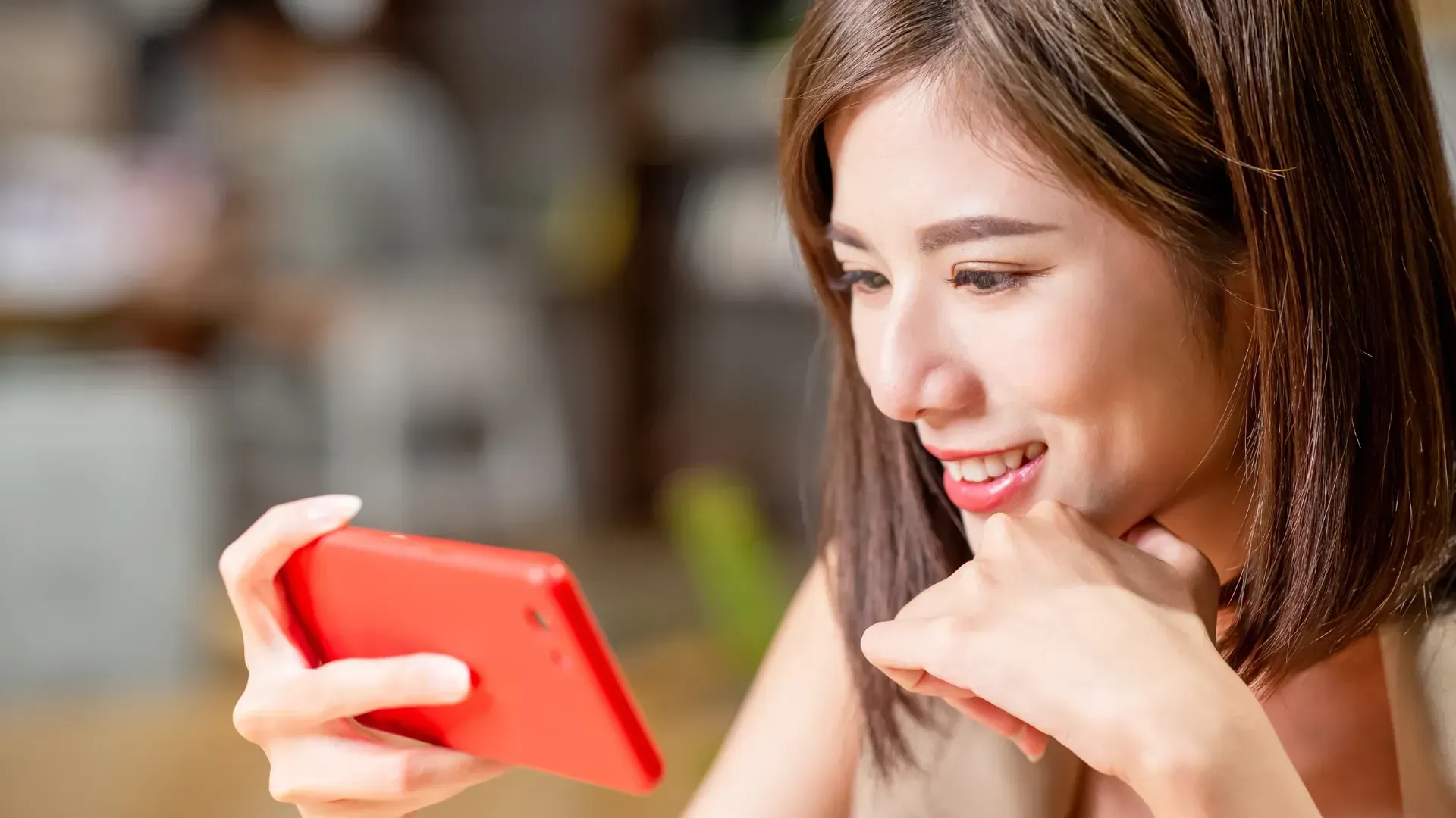 A woman is holding a red cell phone in her hand and smiling.