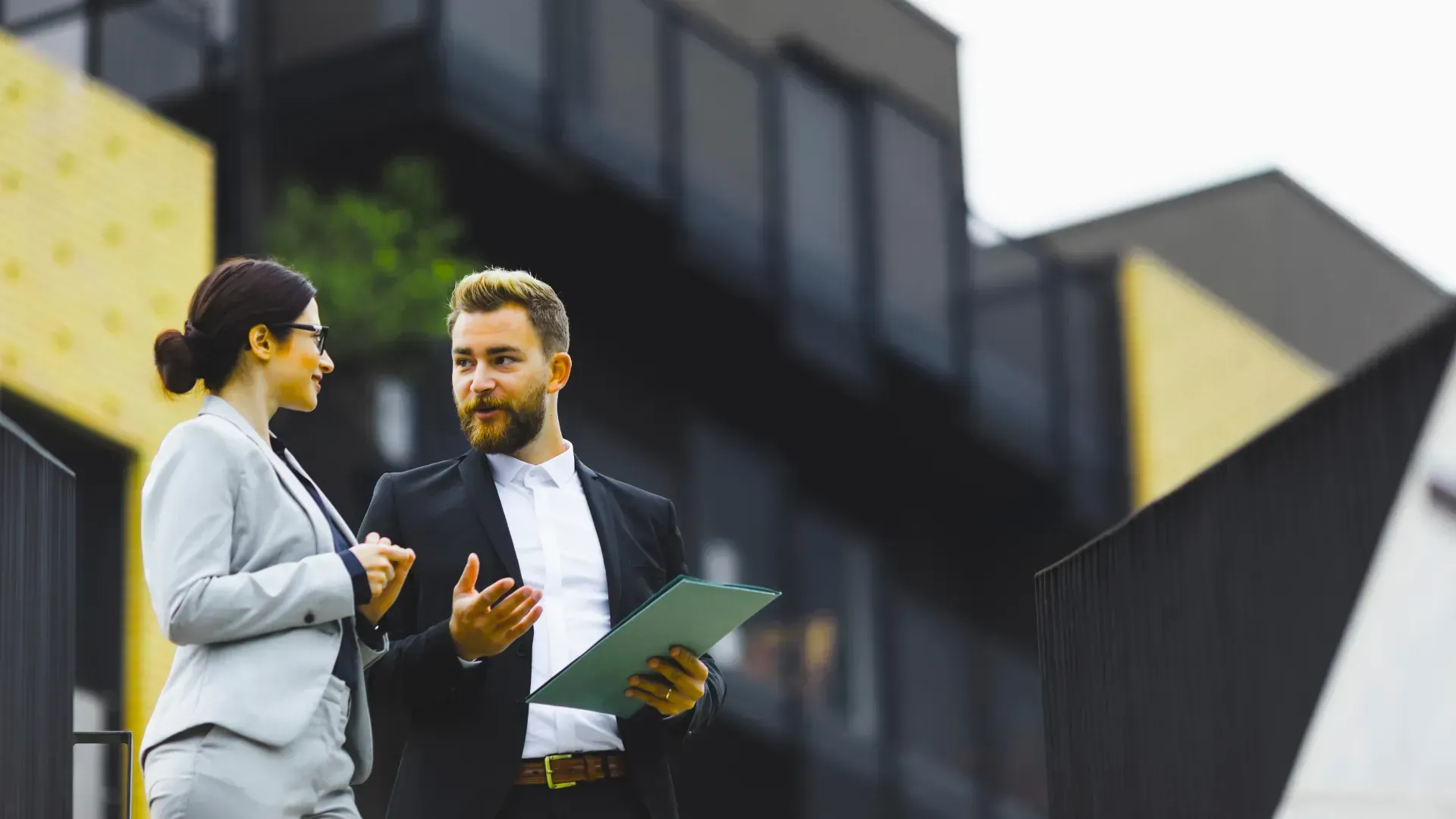 A man and a woman are standing in front of a building talking to each other.