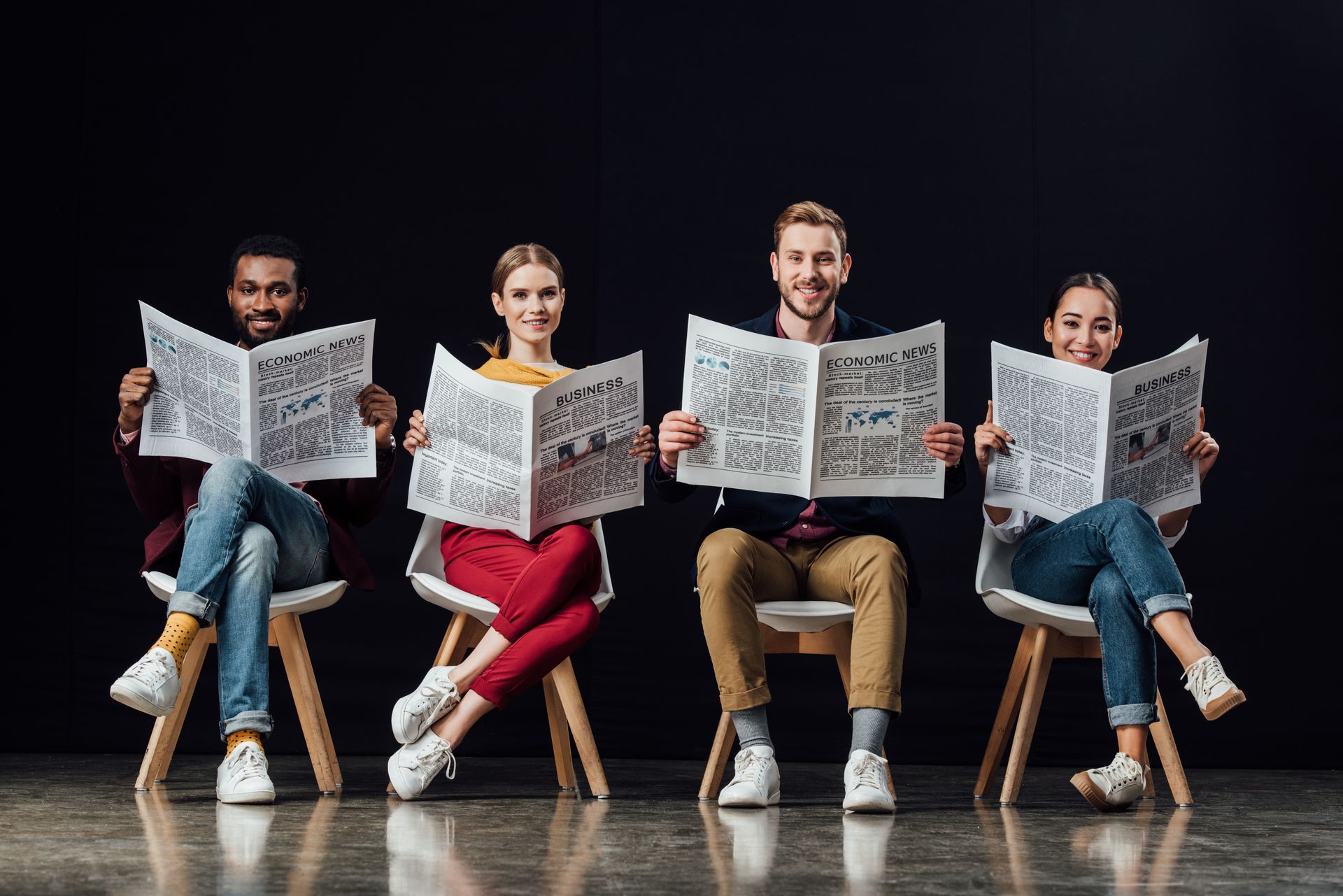A group of people are sitting in chairs reading newspapers.