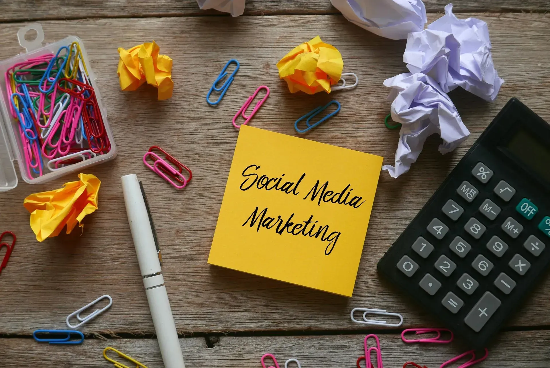 many office objects in a disorganized desk with a note that reads social media marketing