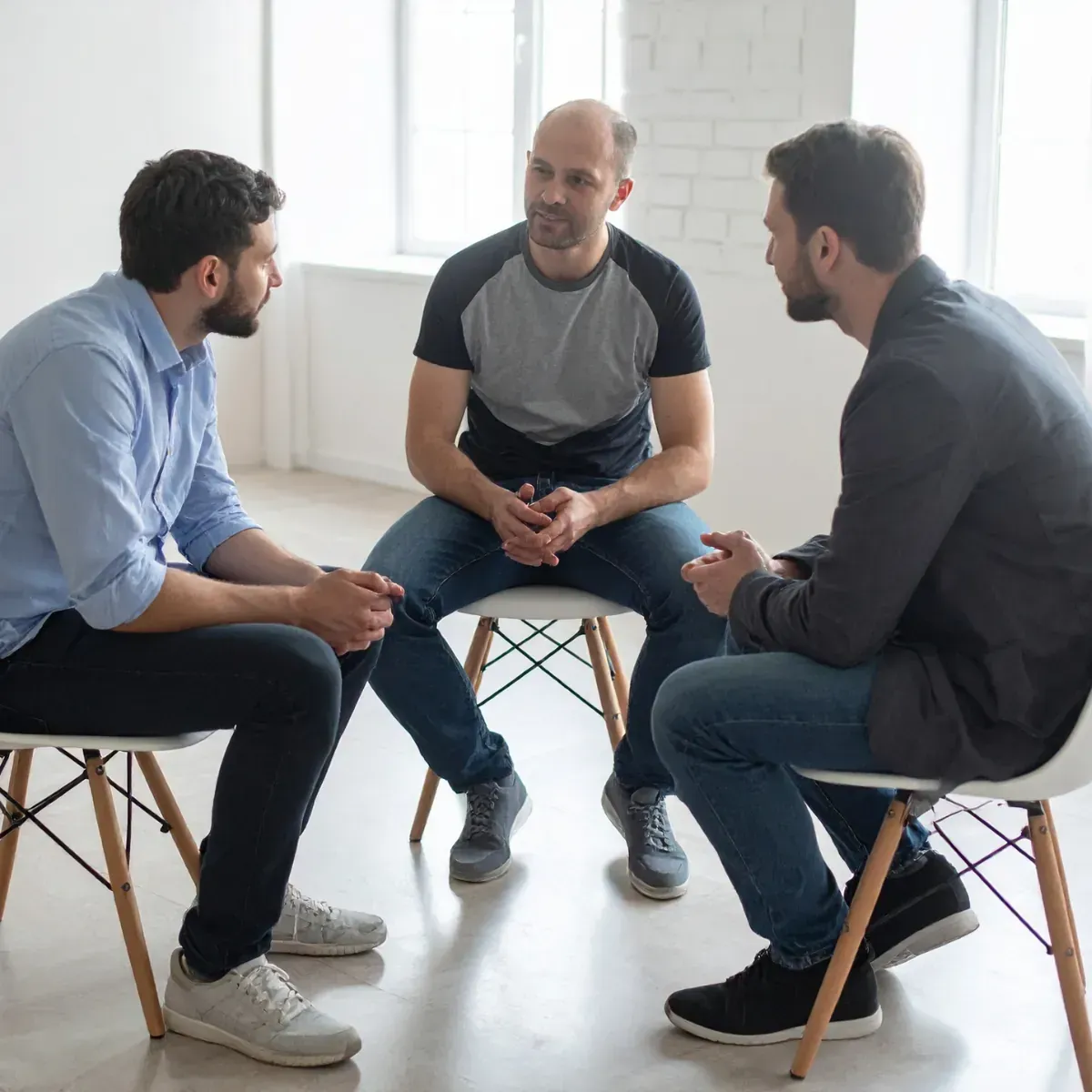 Three men are sitting in chairs in a circle talking to each other.