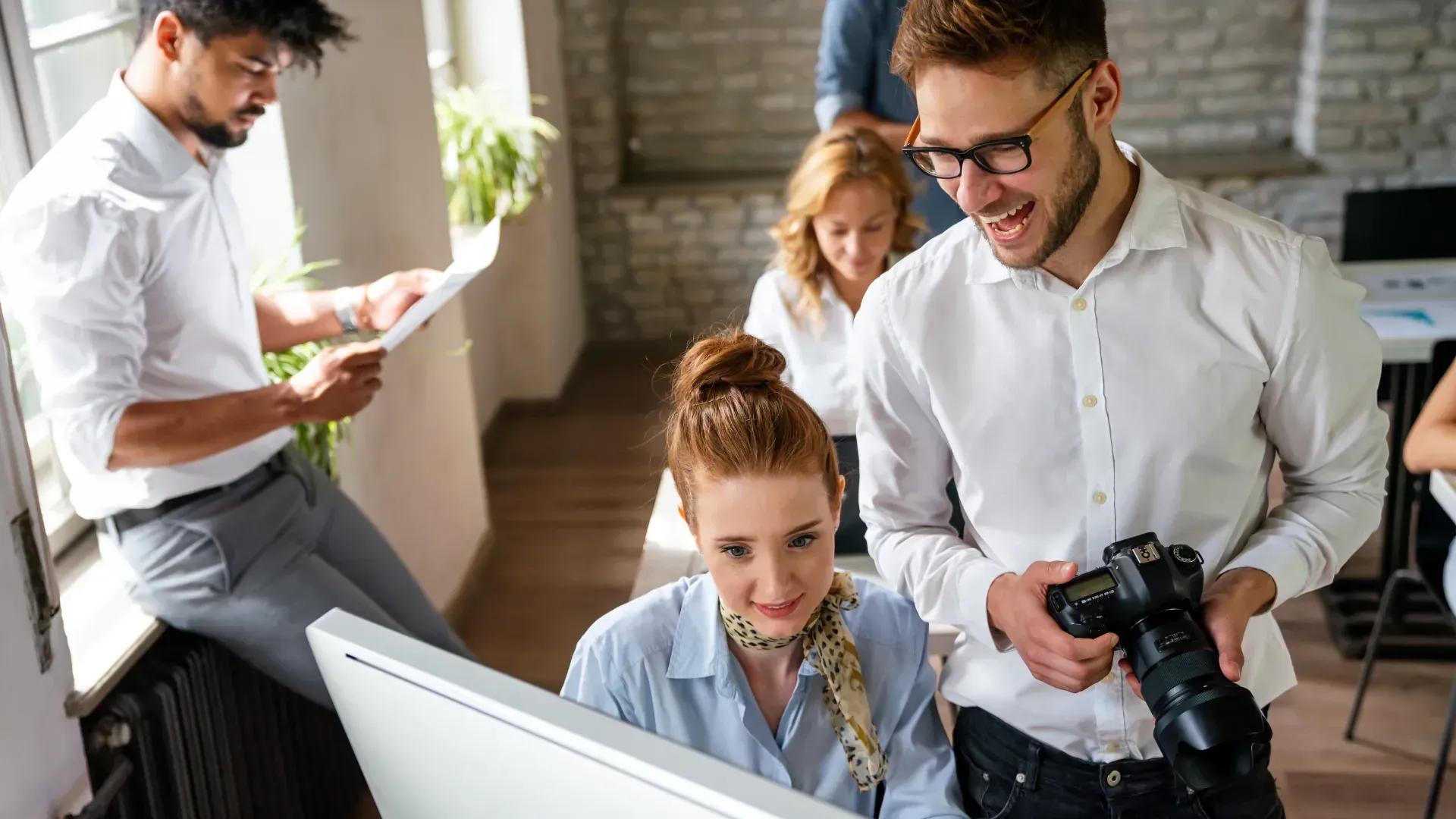A man is holding a camera while a woman looks at a computer screen.