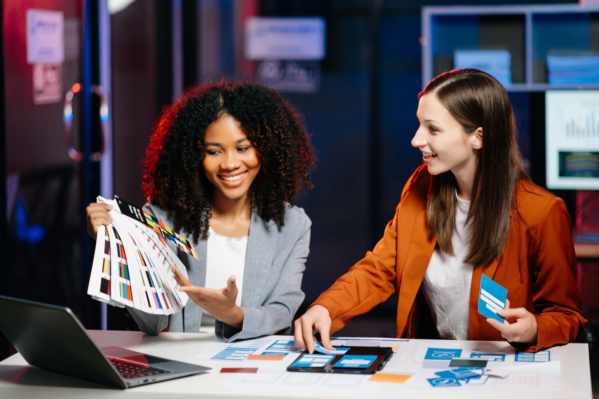 Two women are sitting at a table looking at a laptop.
