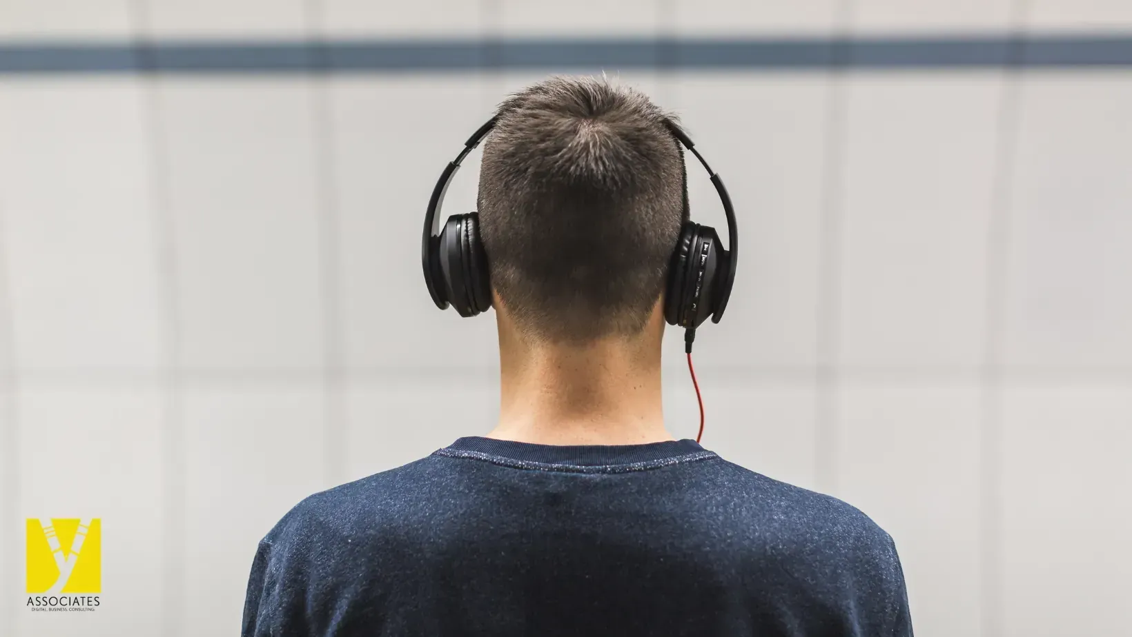 A man wearing headphones is standing in front of a wall.