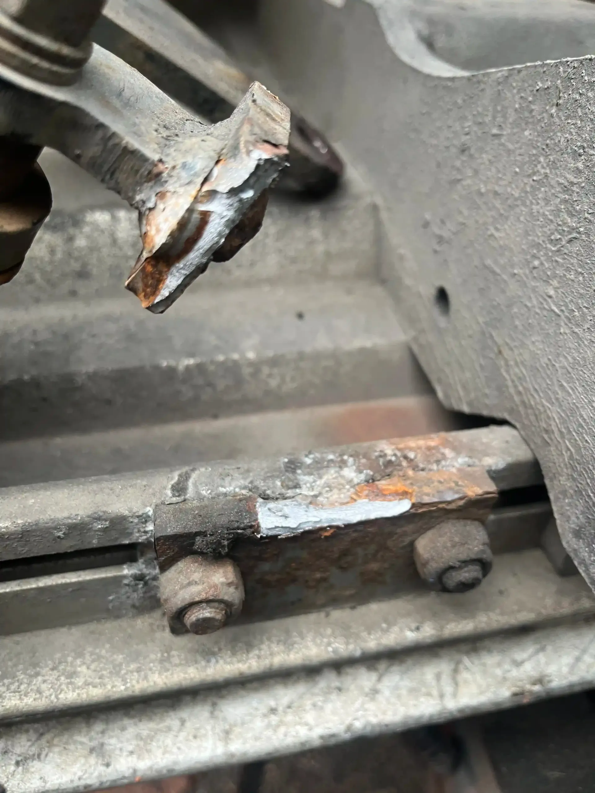 A close-up of a broken metal flange being held over a rusted metal rail with two bolt heads.