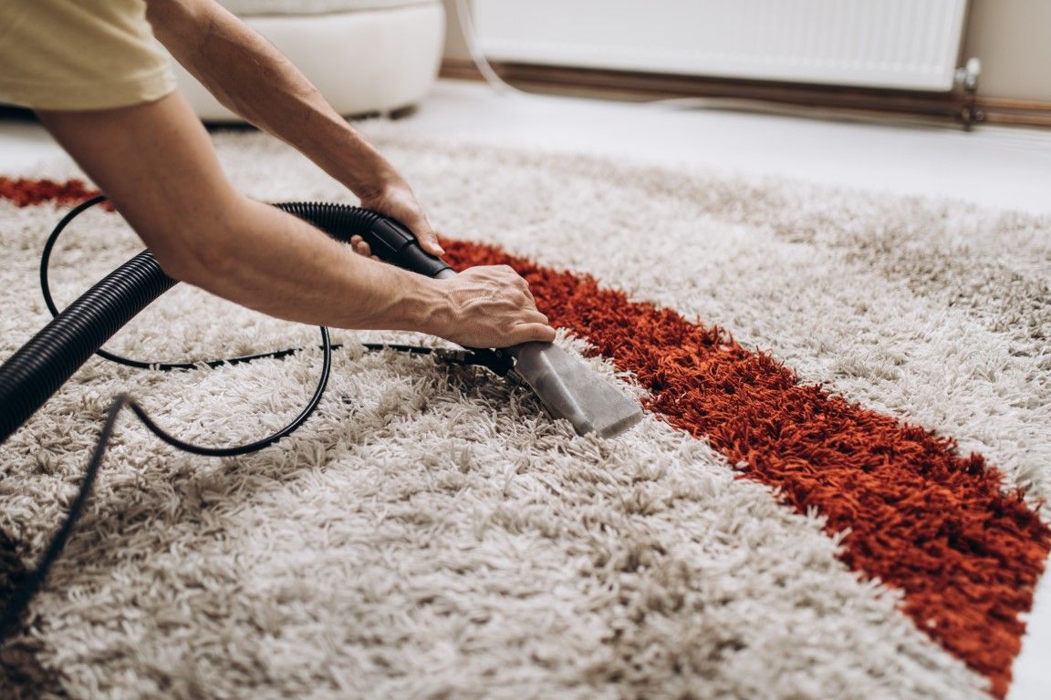 Person cleaning a beige carpet with a vacuum, removing a red stain in a room with a radiator nearby