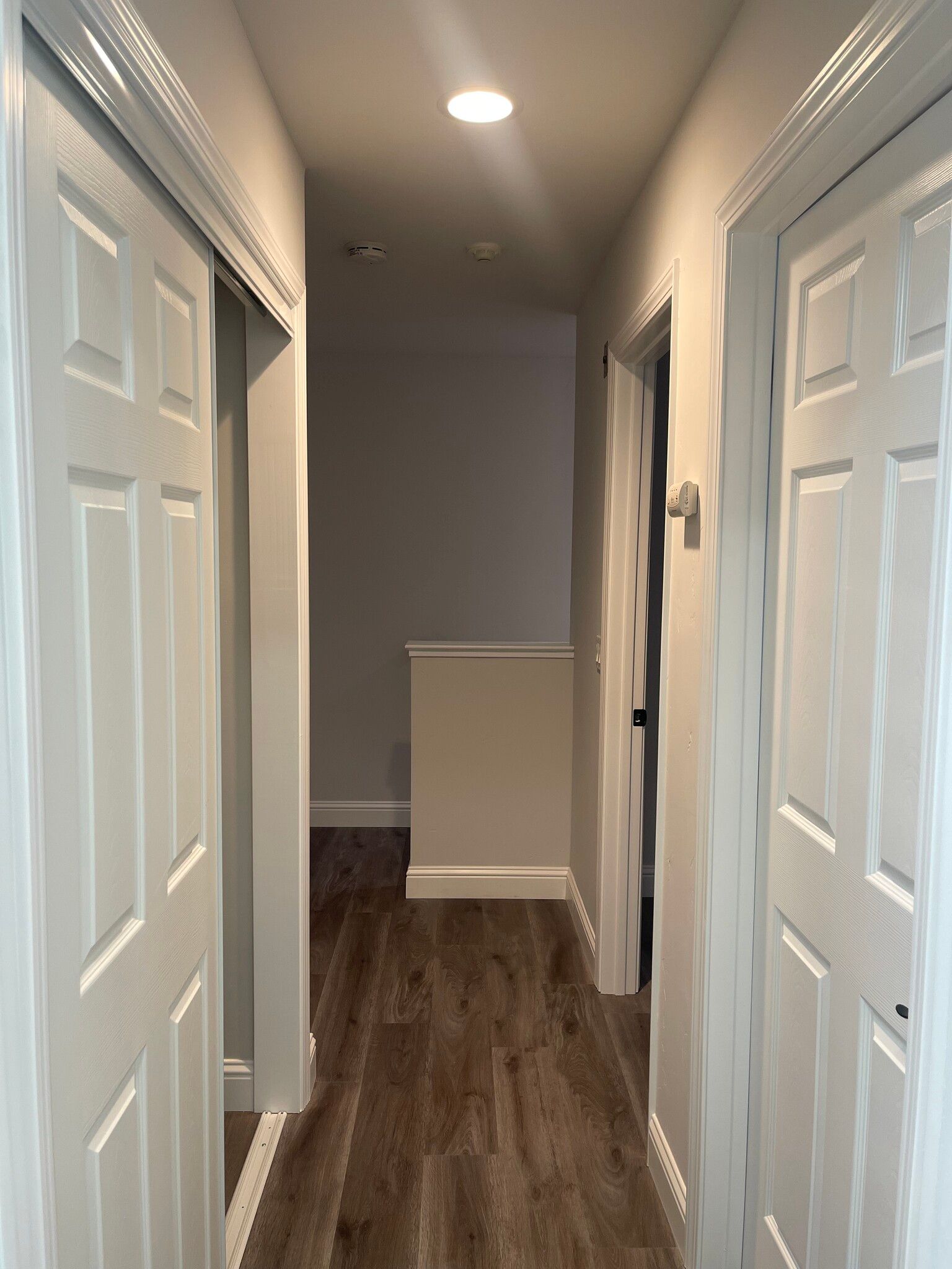 A hallway with white doors and hardwood floors in a house.