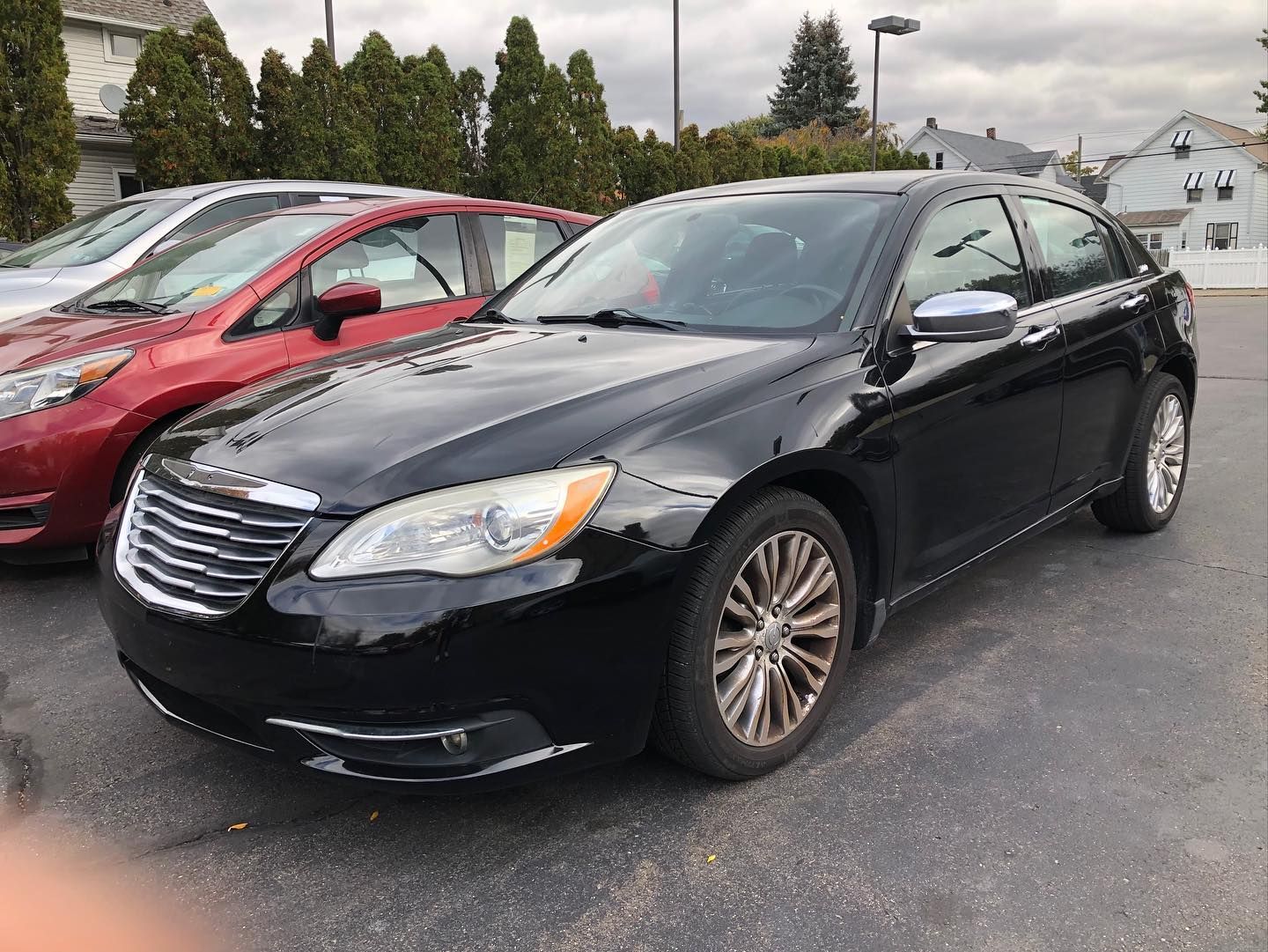 Black Chrysler 200 sedan parked outdoors, next to a red car. The sky is overcast.
