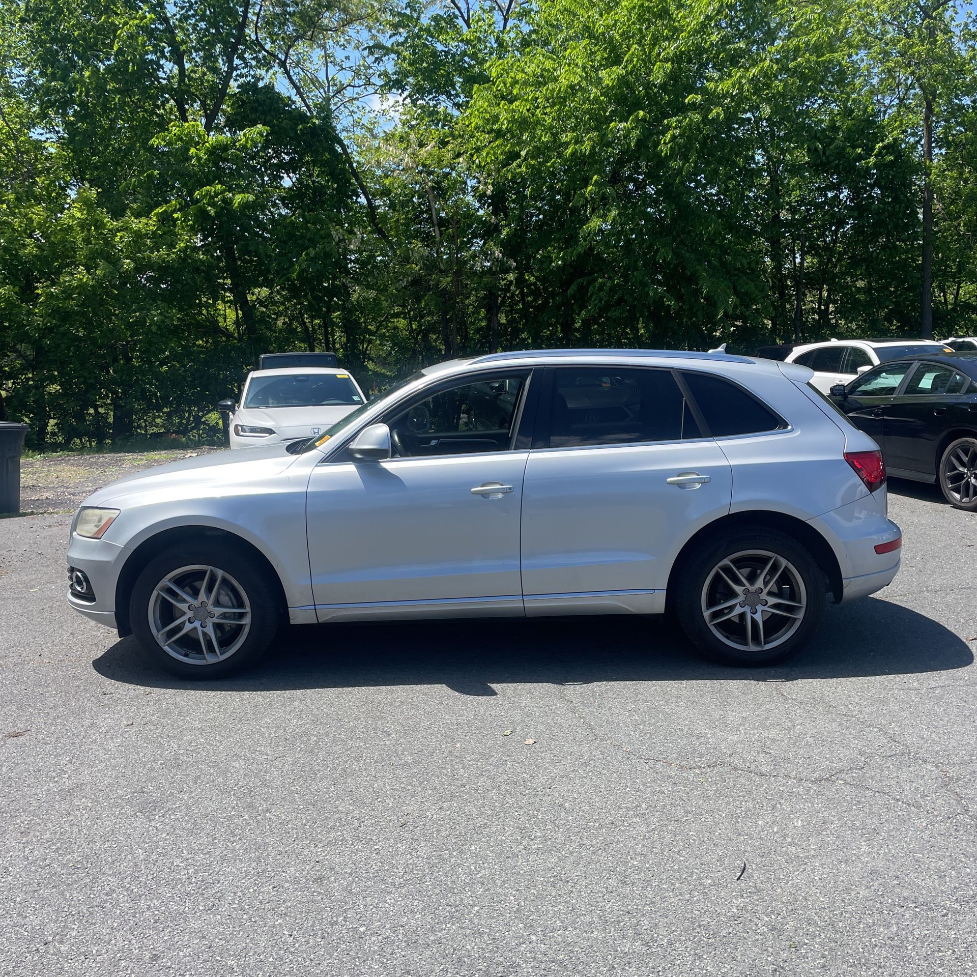 Silver SUV parked on a sunlit lot, side view with trees and other cars in the background