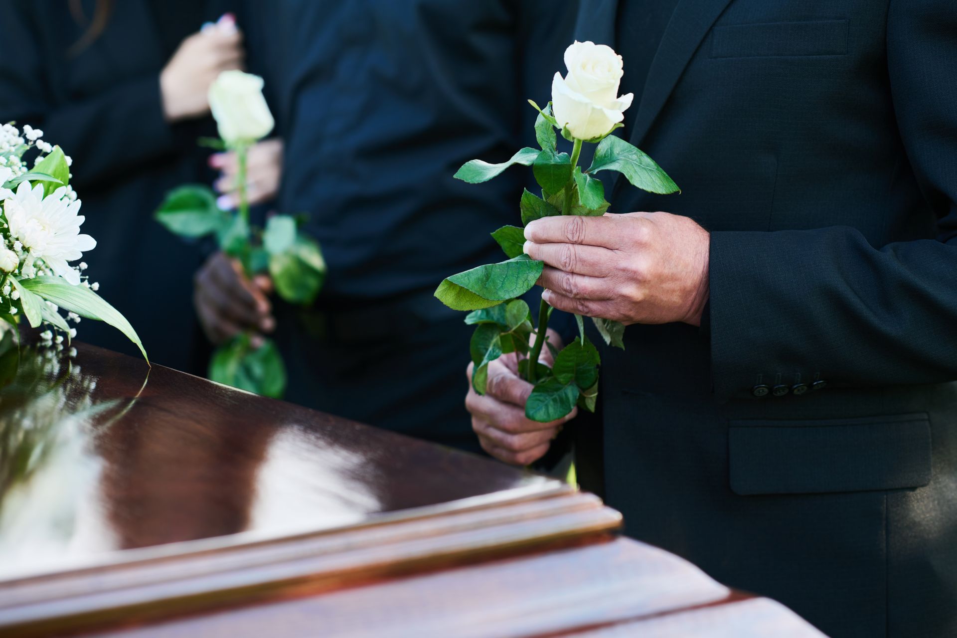 A man in a suit is sitting at a coffin at a funeral.