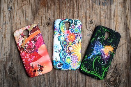 Tre custodie colorate per cellulari su una superficie in legno; ciascuna presenta un esclusivo motivo floreale o astratto.
