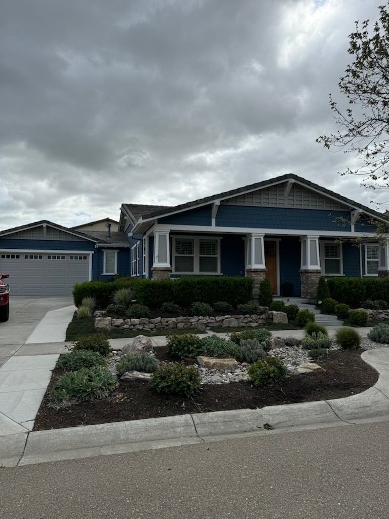 Blue house with gray trim and garage, front yard with landscaping under a cloudy sky.