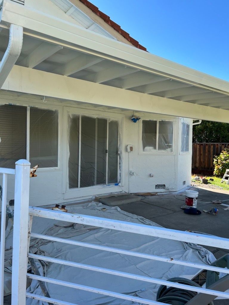 Exterior of a house being painted white. Sliding glass doors and a covered patio are visible.