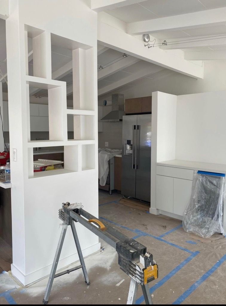 White room undergoing renovation with partially constructed shelving and kitchen visible. White room undergoing renovation with partially constructed shelving and kitchen visible.