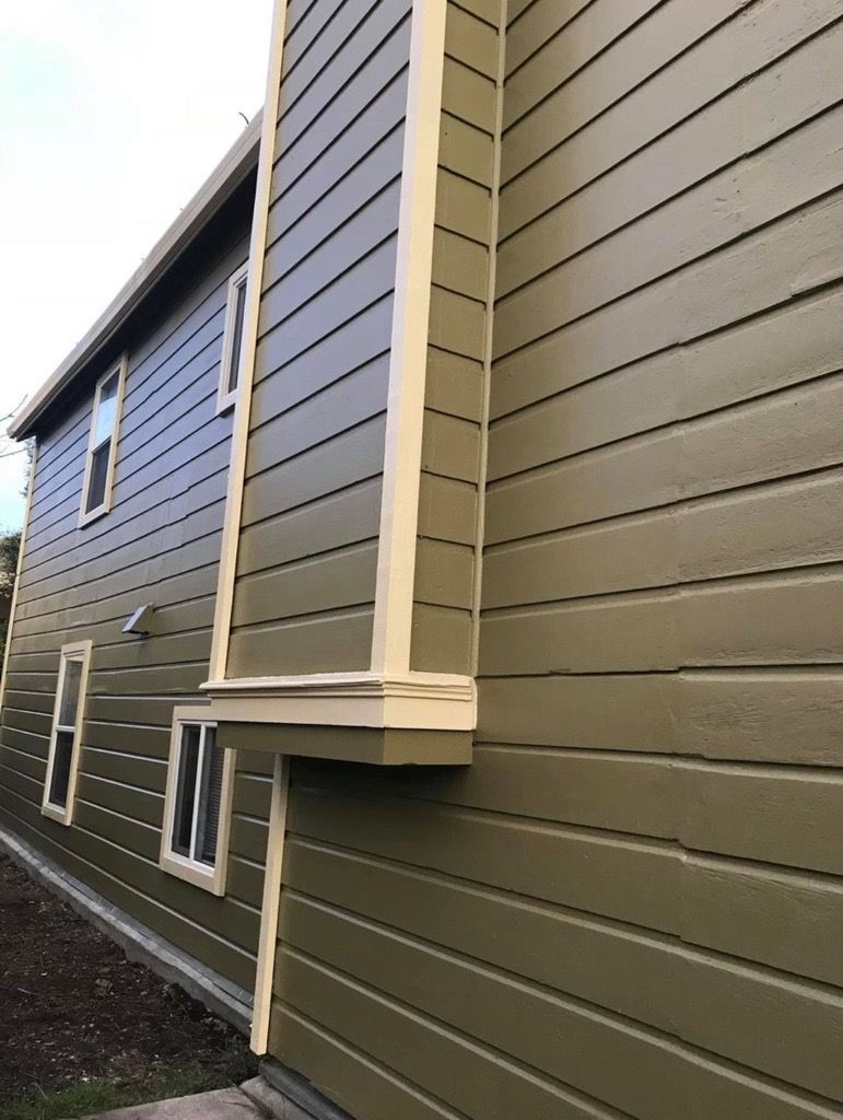 Exterior of a two-story building with green siding and cream trim. Windows and a small ledge are visible.