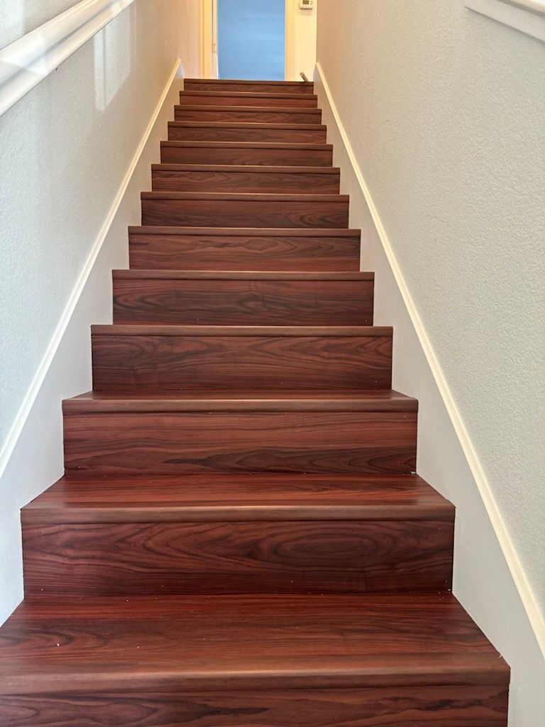 Wooden staircase ascending, framed by white walls and handrail, leading upwards towards a doorway.