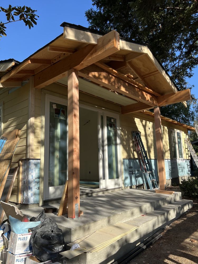 House under construction with a porch. Light yellow siding, exposed wood framing, concrete steps. House under construction with a porch. Light yellow siding, exposed wood framing, concrete steps.