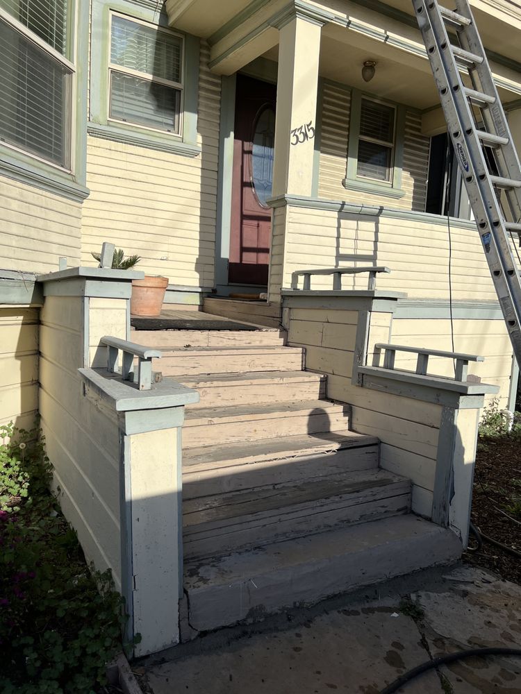 Front steps of a house with weathered concrete and railings, a ladder, and a partially open door. Front steps of a house with weathered concrete and railings, a ladder, and a partially open door.