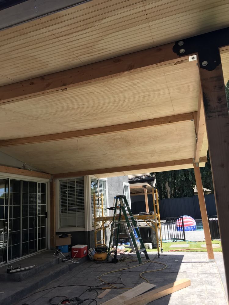 Person staining a wood ceiling from the ground using a long-handled applicator on a building exterior.