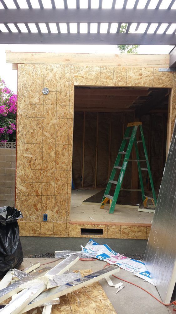 Construction site: exterior wall with open doorway, green lad der inside.