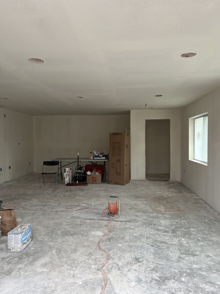 Empty, unfinished room with concrete floor, white walls, and recessed lighting. A door and a window are visible.