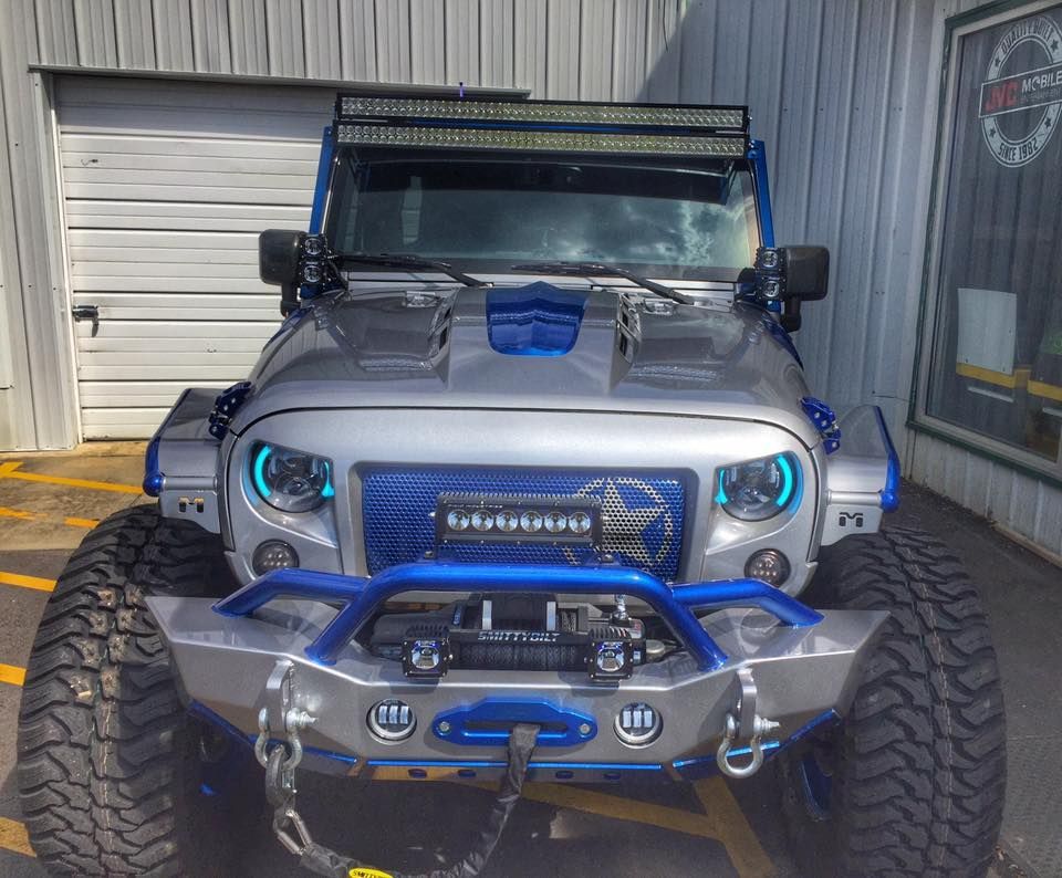Blue off-road Jeep with large tires and winch parked in a garage, front view