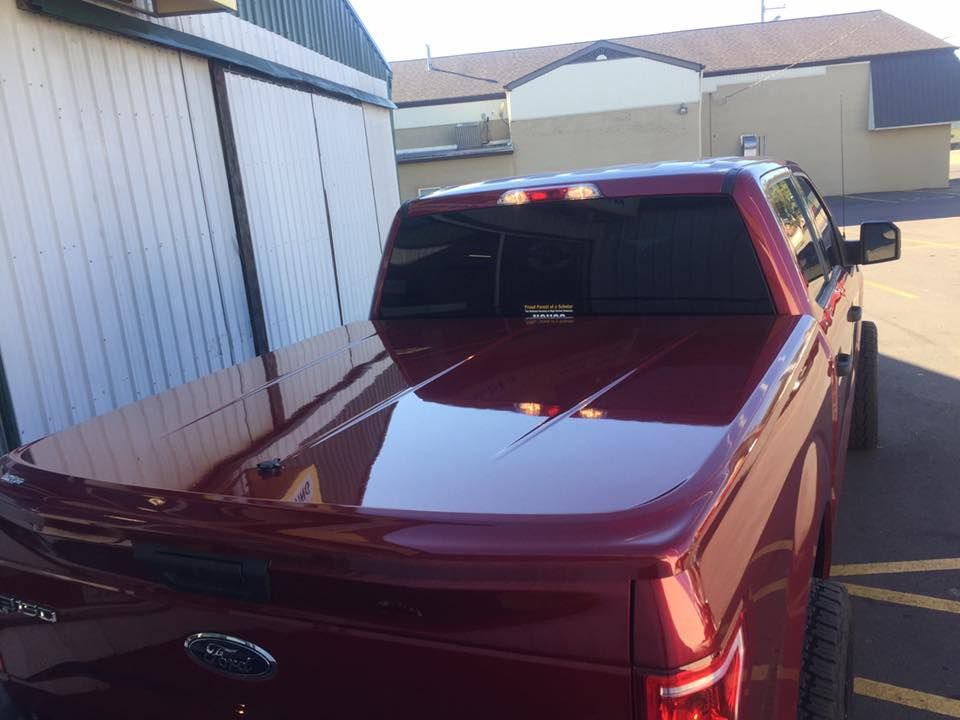 Red Ford pickup truck parked beside a white building in a driveway.