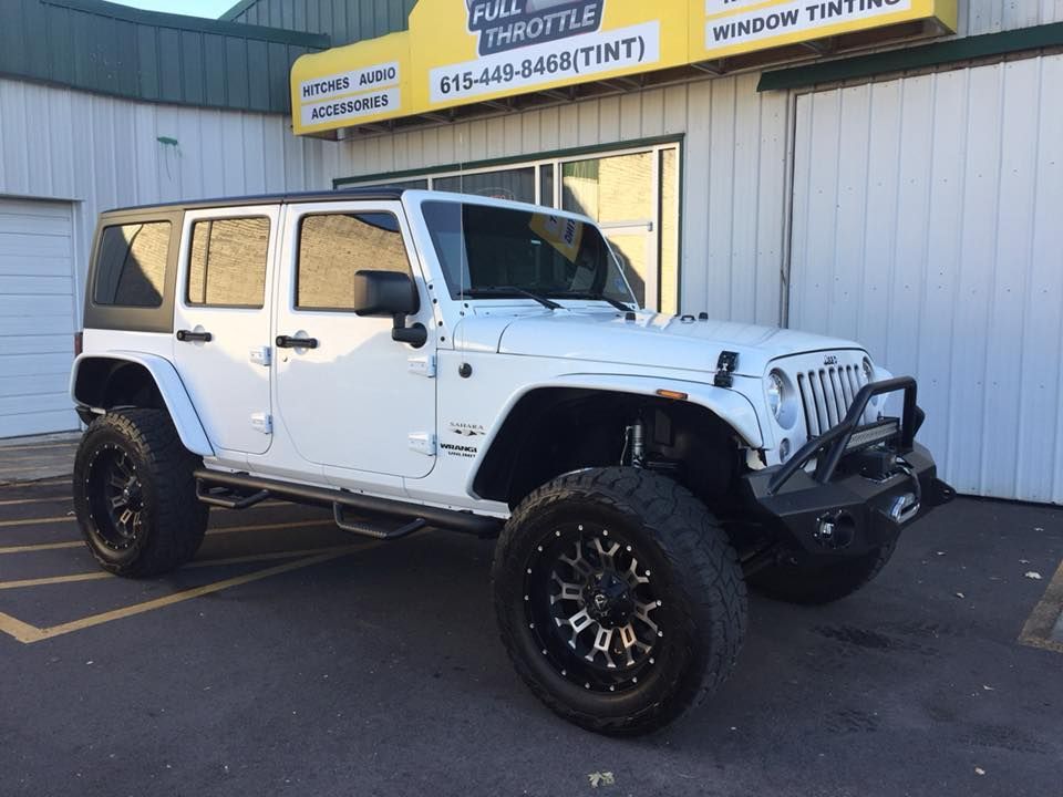 White Jeep Wrangler parked outside a shop, with lifted suspension and black wheels