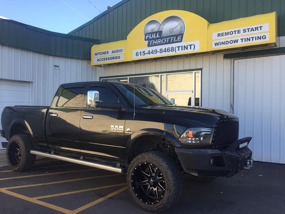 Black lifted pickup truck parked outside an auto shop with yellow signage.