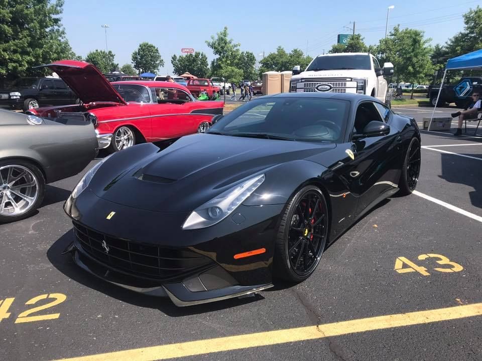 Black Ferrari parked in a lot beside other cars, with the number 43 painted on the ground.