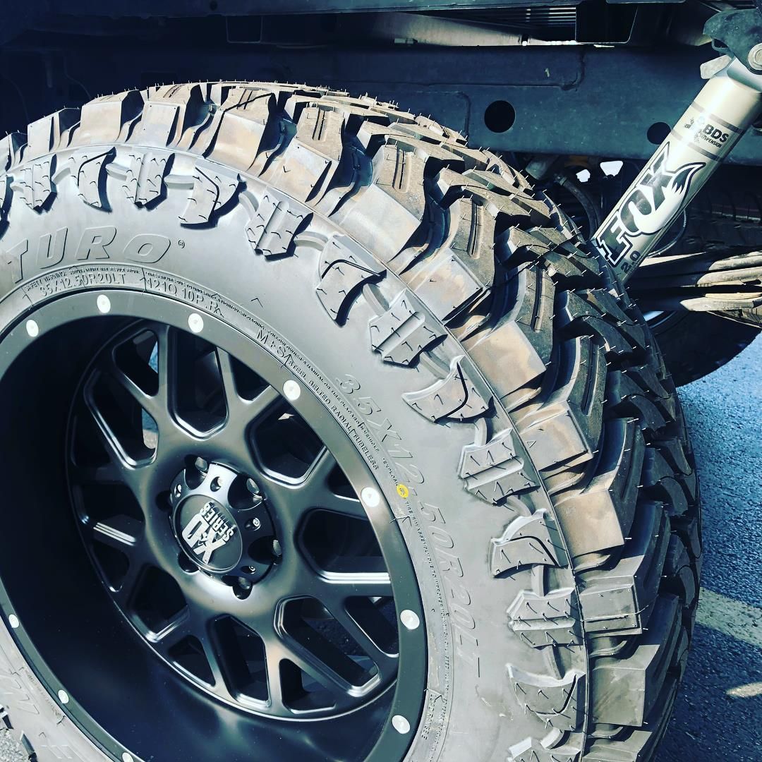 Close-up of an off-road truck tire with deep tread and a black alloy wheel