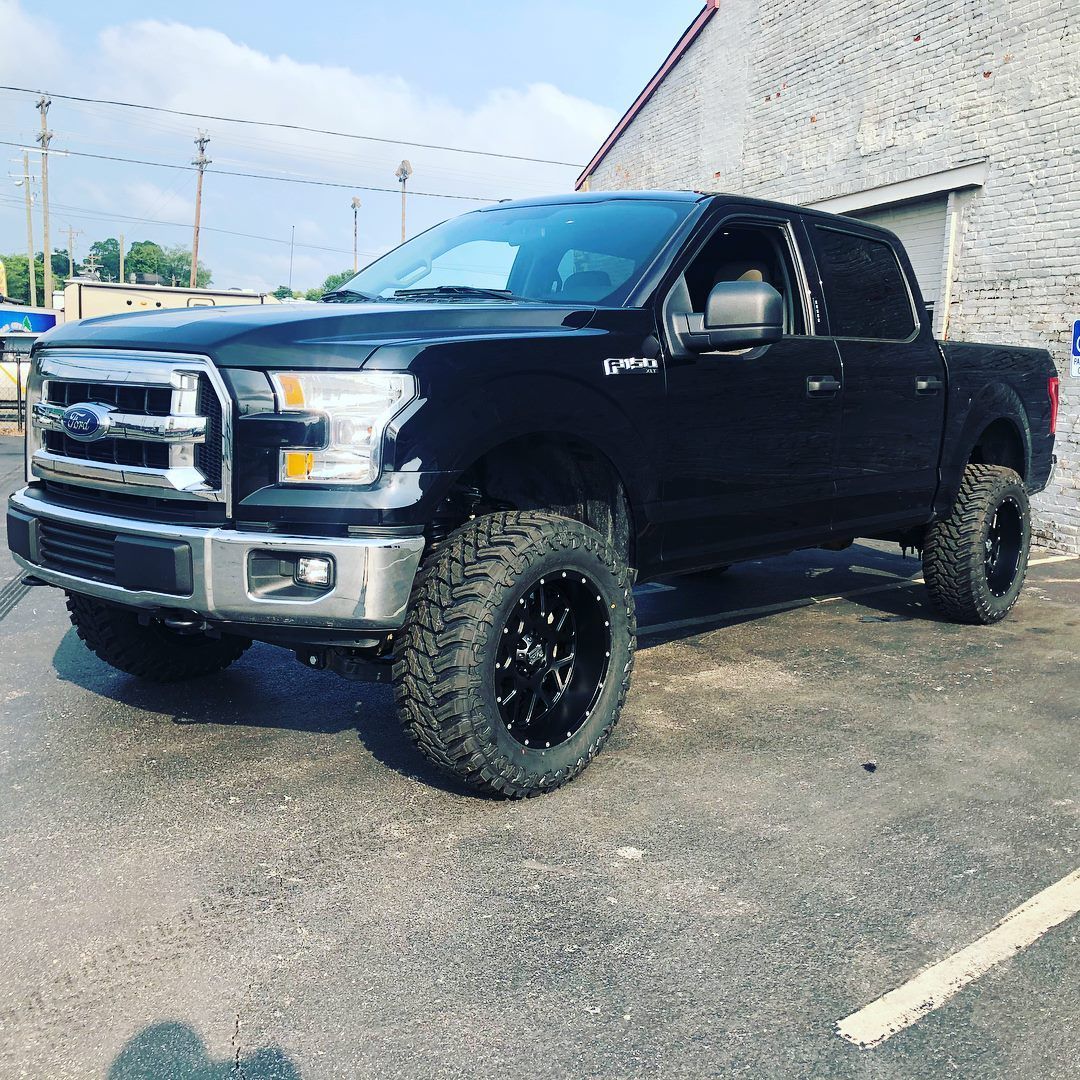 Black lifted pickup truck parked beside a building on a sunny day