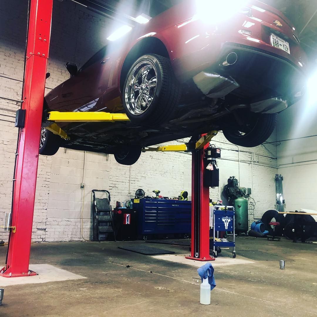 Car lifted on a red auto repair lift inside a garage, with tools and equipment nearby